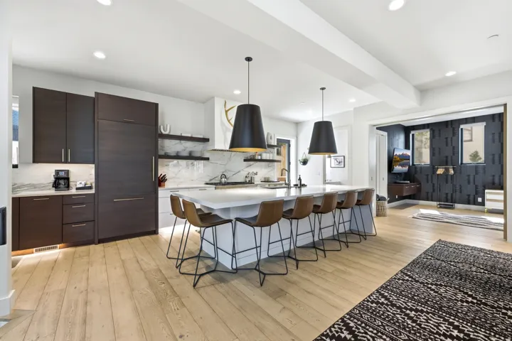Contemporary kitchen featuring a large central island, light wood-finish flooring, dark wood cabinetry, integrated appliances, and a marble-patterned backsplash