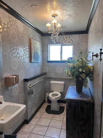 Powder room featuring a crystal chandelier, patterned wallpaper, wall-mounted sink, and a built-in window providing natural light