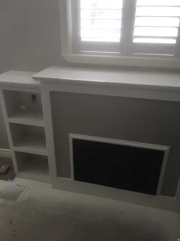 Built-in cabinetry featuring shelving and a decorative inset panel, complemented by a window with white plantation shutters and detailed trim work