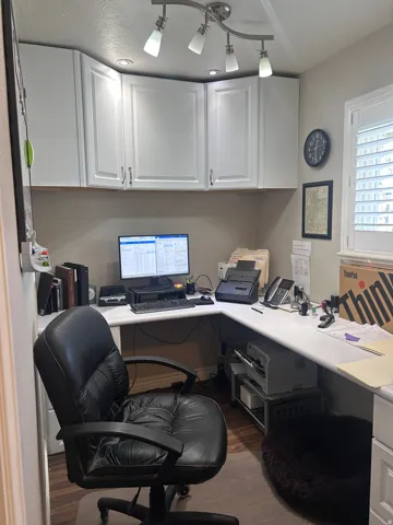 Dedicated workspace featuring white cabinetry with brushed nickel hardware, an L-shaped desk, recessed lighting, track lighting, and wood-finish flooring