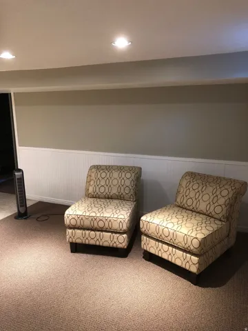 Recessed ceiling lighting illuminates a room featuring a neutral wall color, white wainscoting, and brown carpet flooring