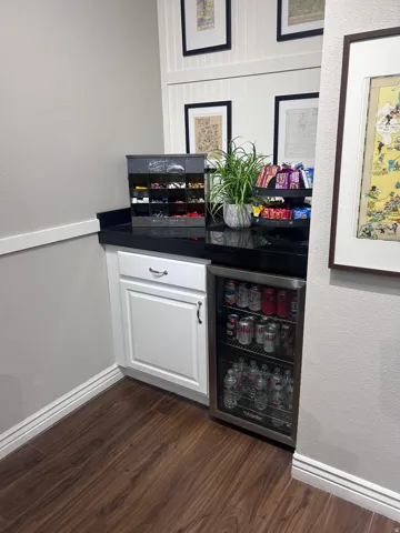 Built-in beverage station featuring white cabinetry, a dark countertop, an under-counter refrigerator, wood-finish flooring, and wainscoting