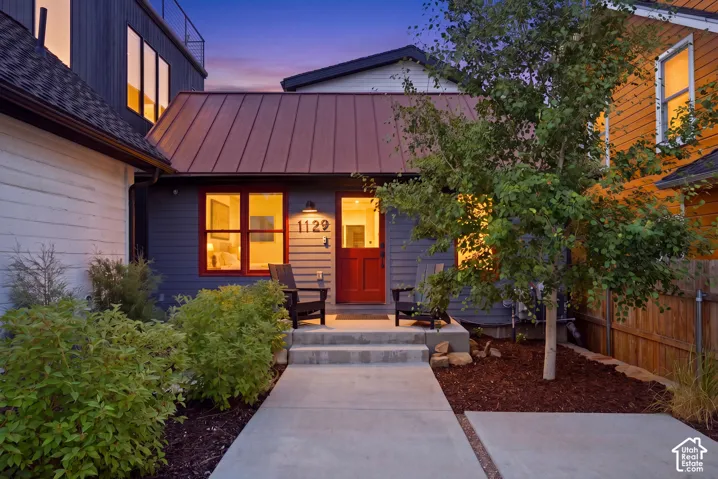 Front entry with a concrete walkway, red door, and a metal roof