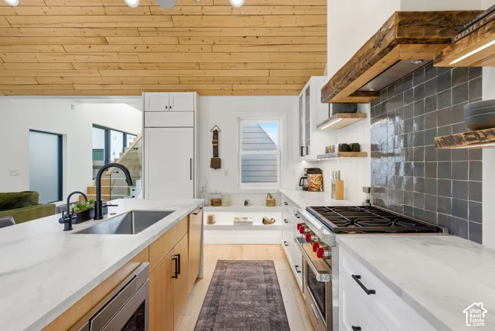 Open-concept kitchen featuring a wood-panel ceiling, full-size refrigerator, gas range, and a central island with an undermount sink and matte black faucet