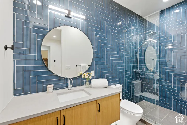 Bathroom featuring a blue herringbone tile accent wall, glass-enclosed shower, wood-finish vanity with an integrated sink, a rectangular light fixture, and a circular mirror