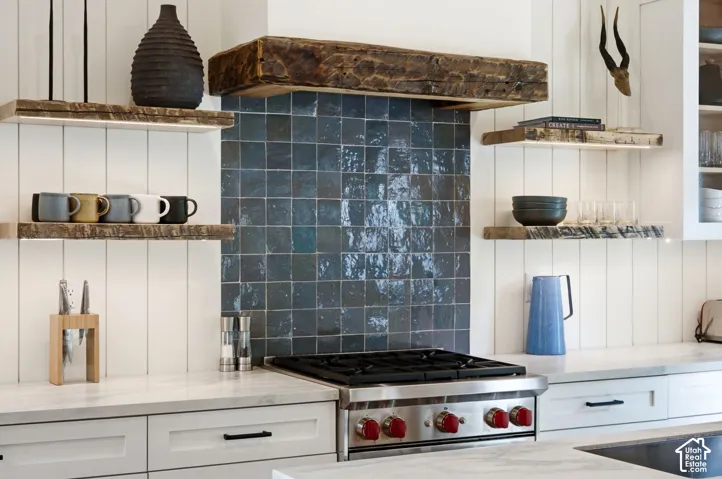 Gourmet kitchen featuring a stainless steel range with red accents, a rich blue tiled backsplash, and a rustic wood range hood