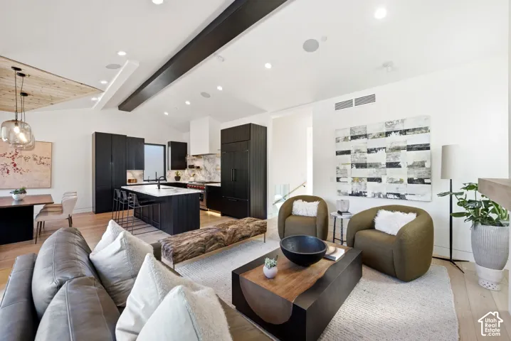 Open-concept living space featuring vaulted ceilings with exposed beams, light wood-finish flooring, and recessed lighting