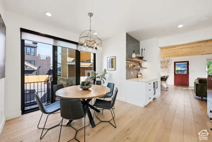 Open-concept living area with light wood-finish flooring, a built-in wet bar featuring a beverage cooler and floating shelves, and a full-height glass sliding door with a balcony