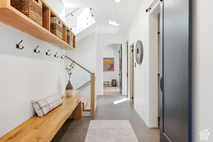 Entryway featuring a built-in wood bench with overhead shelving and coat hooks, a glass and wood-finish staircase railing, a dark gray barn door, and tile flooring
