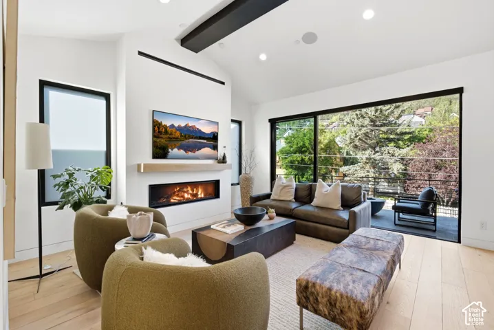 Spacious living area featuring light wood-finish flooring, a contemporary linear fireplace with a light wood mantle, recessed lighting, and a large sliding glass door opening to an outdoor balcony