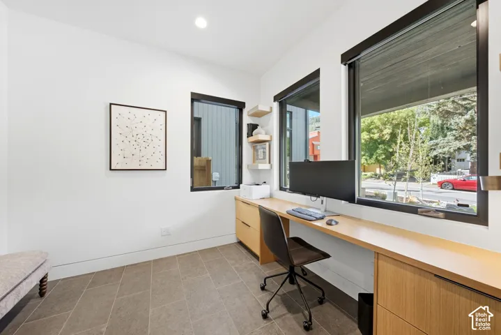 Integrated built-in desk with wood-finish cabinetry, gray tile flooring, recessed lighting, and expansive windows