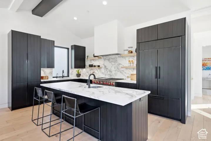 Gourmet kitchen featuring a waterfall island with stone countertops, panel-front refrigerator, black wood-finish cabinetry, and a stone backsplash