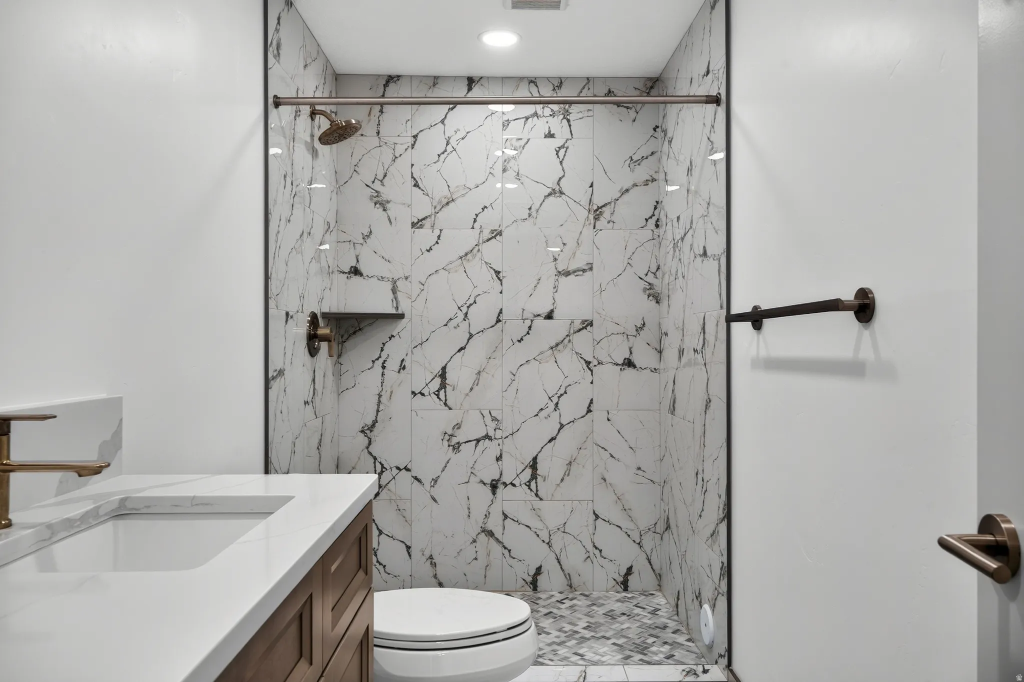 Bathroom featuring a walk-in shower with marble-look tile walls, a built-in shower niche, and a mosaic tile floor
