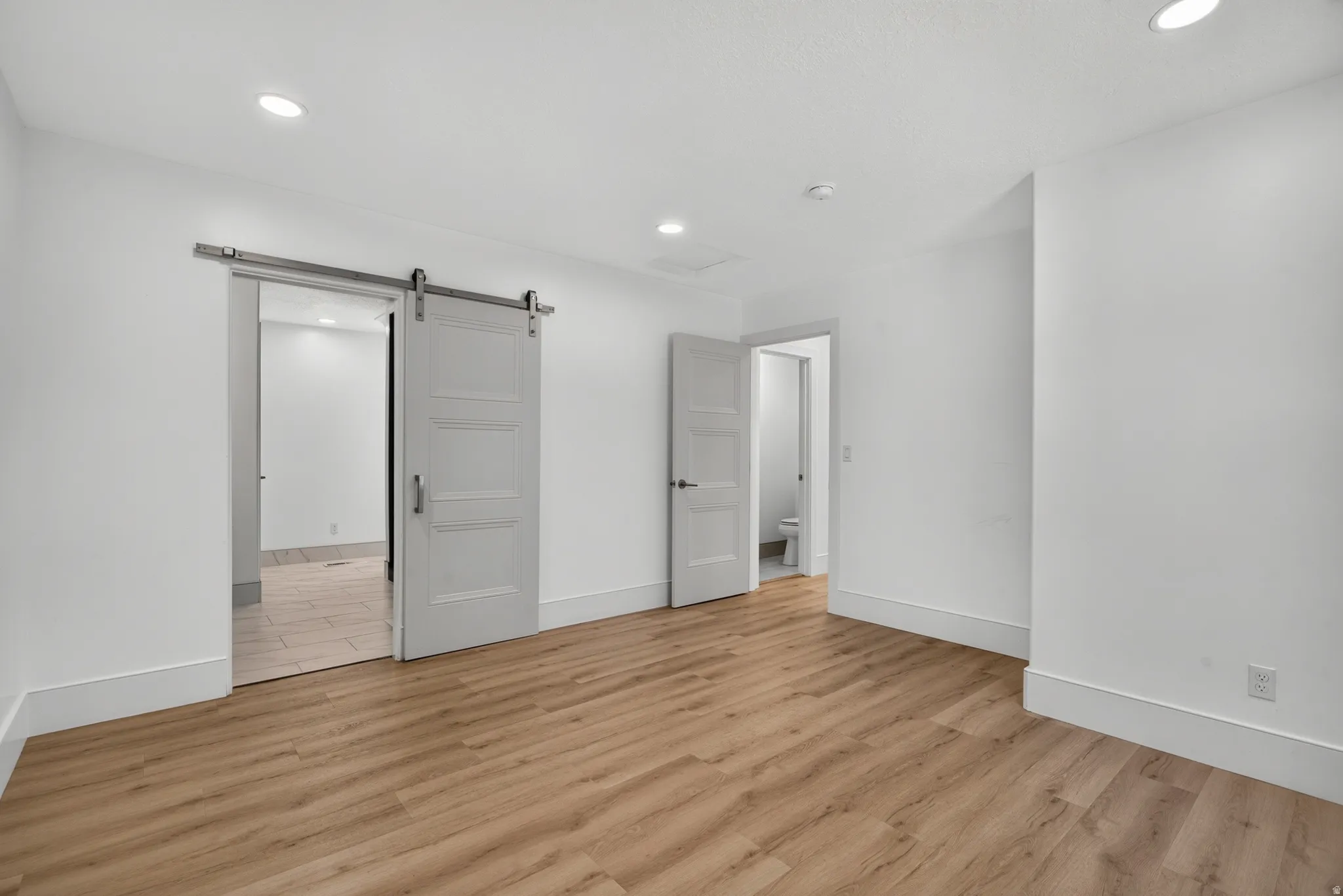 Spacious room featuring wood-finish flooring, white walls, and recessed lighting