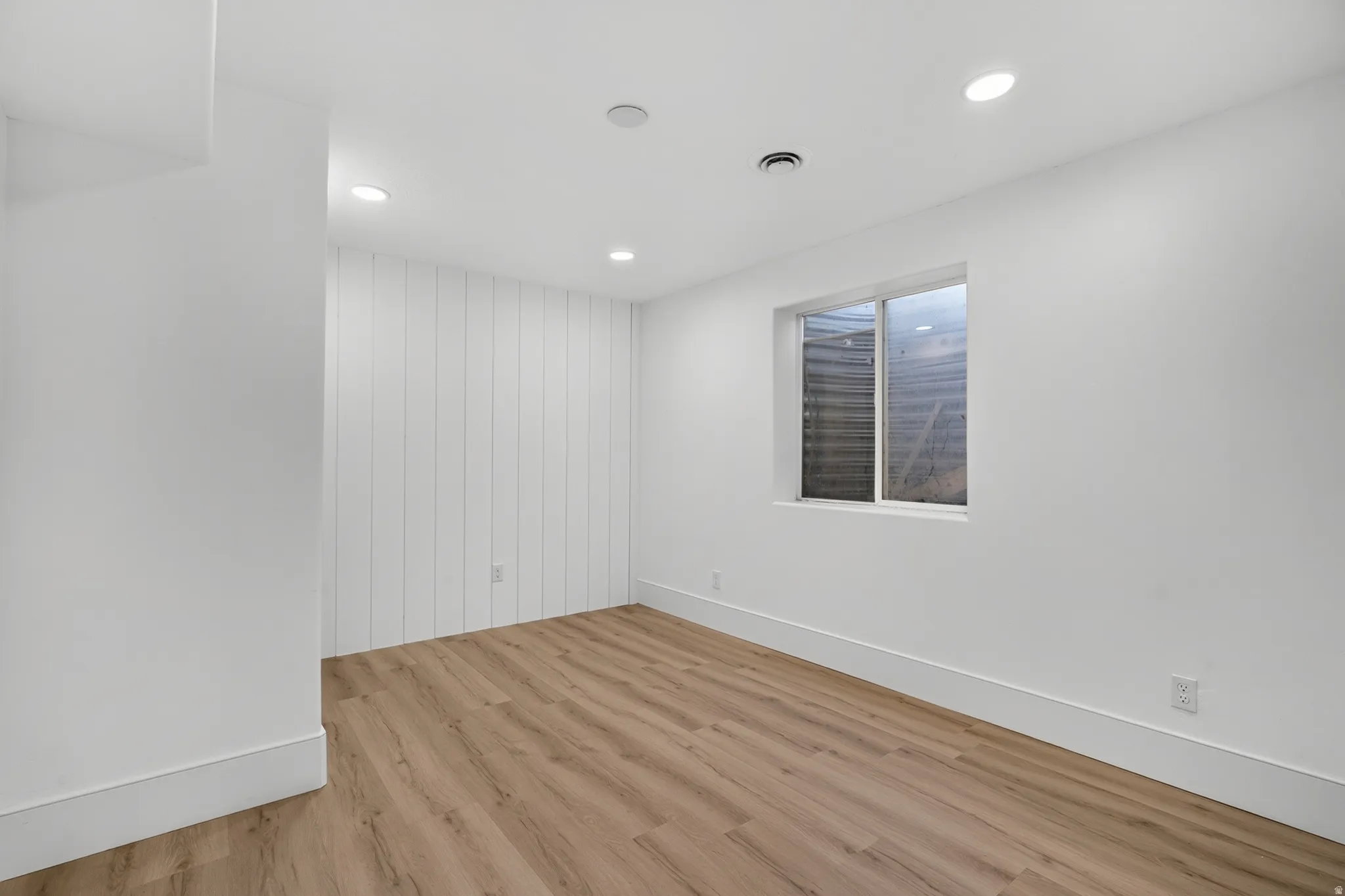Spacious room featuring wood-finish flooring, recessed lighting, and a window providing natural illumination