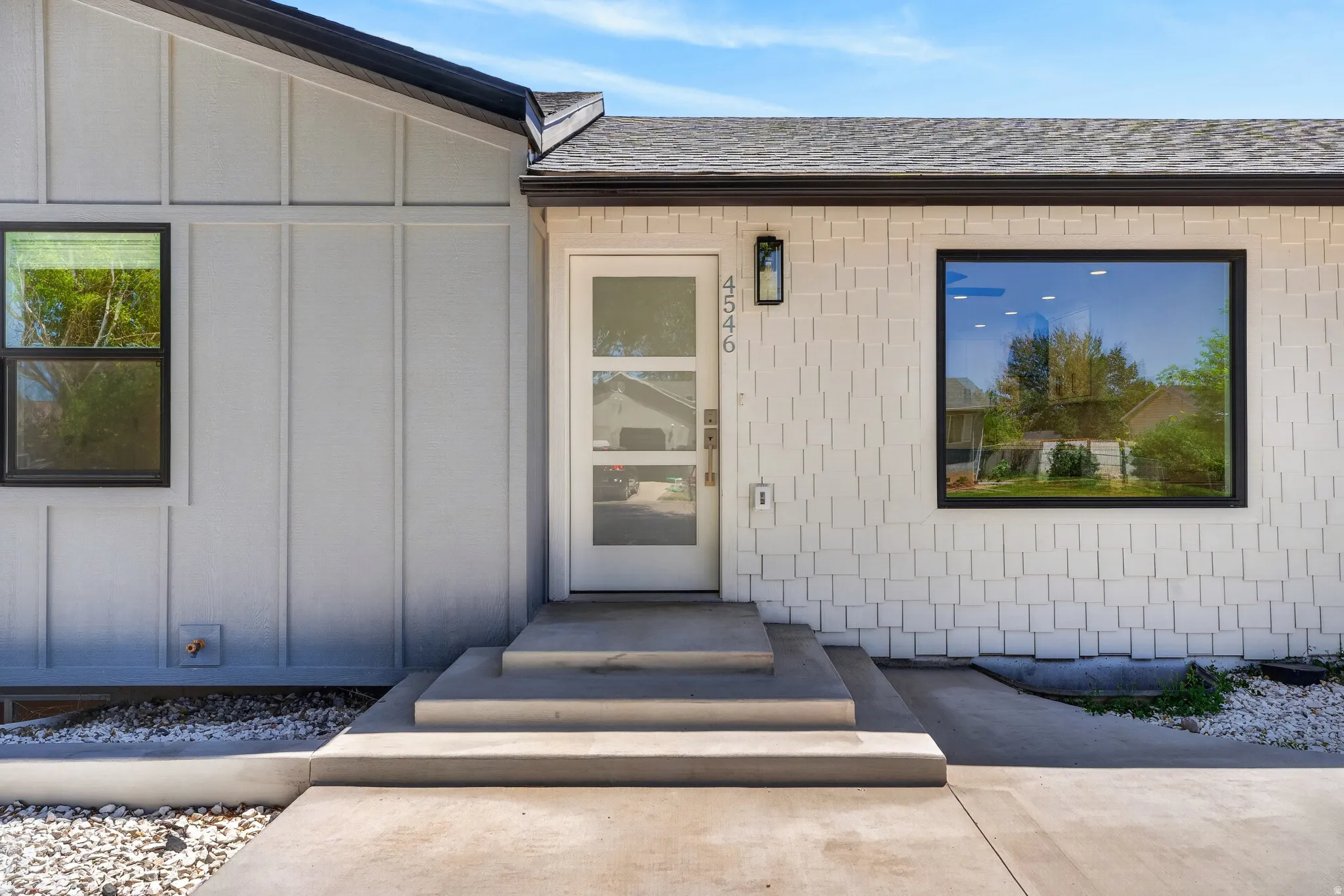 Modern exterior featuring board and batten siding, shake siding, a glass-panel entry door, and dark-framed windows