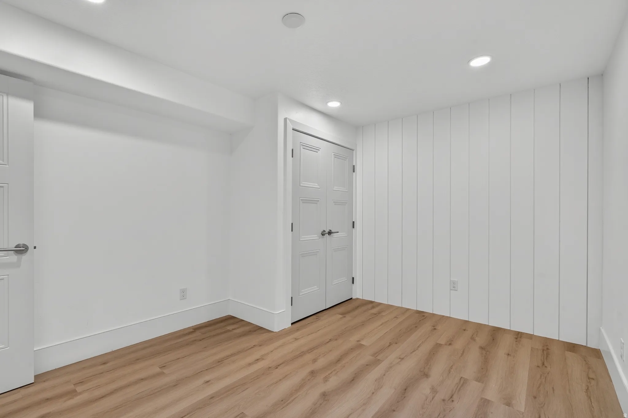 Room featuring wood-finish flooring, recessed lighting, white trim, a shiplap accent wall, and paneled doors