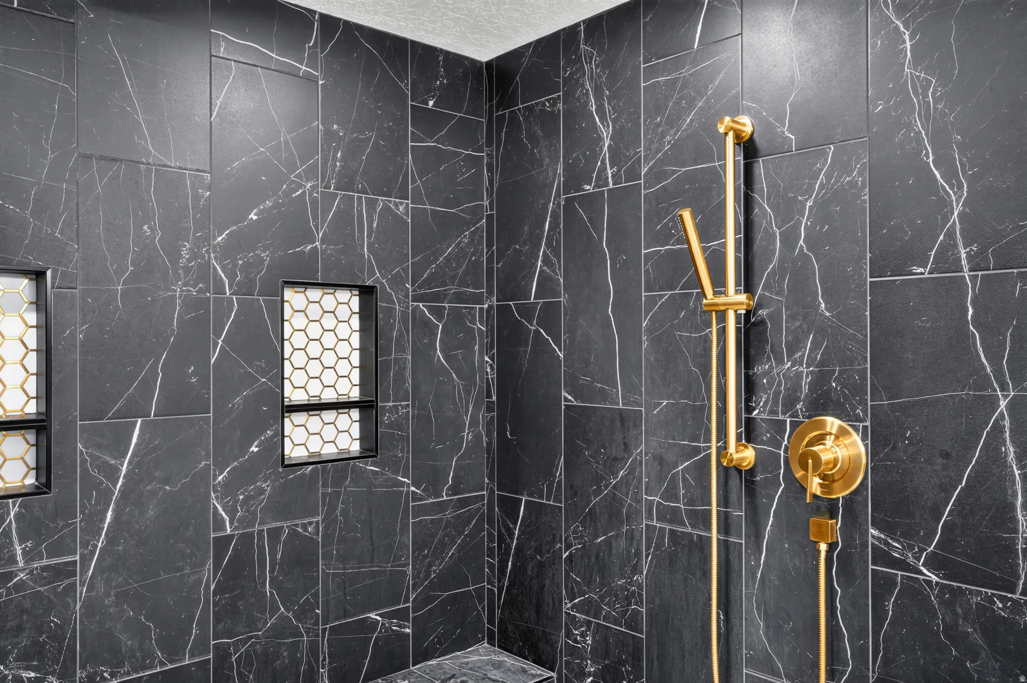 Shower enclosure featuring dark marbled tile, two recessed niches with hexagonal mosaic tile, a built-in shower bench, and gold-finish fixtures