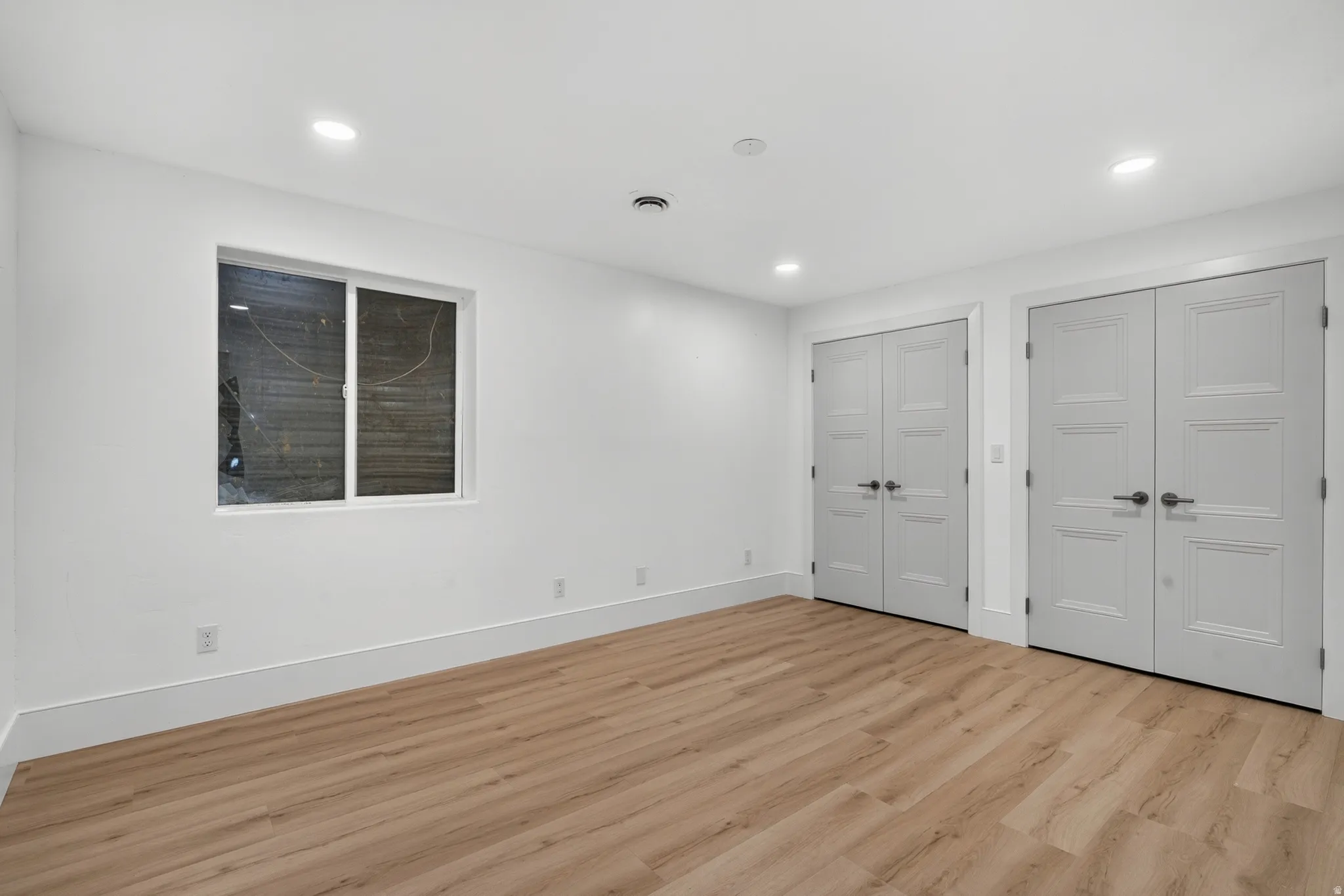 Spacious room featuring light wood-finish flooring, recessed lighting, and white walls