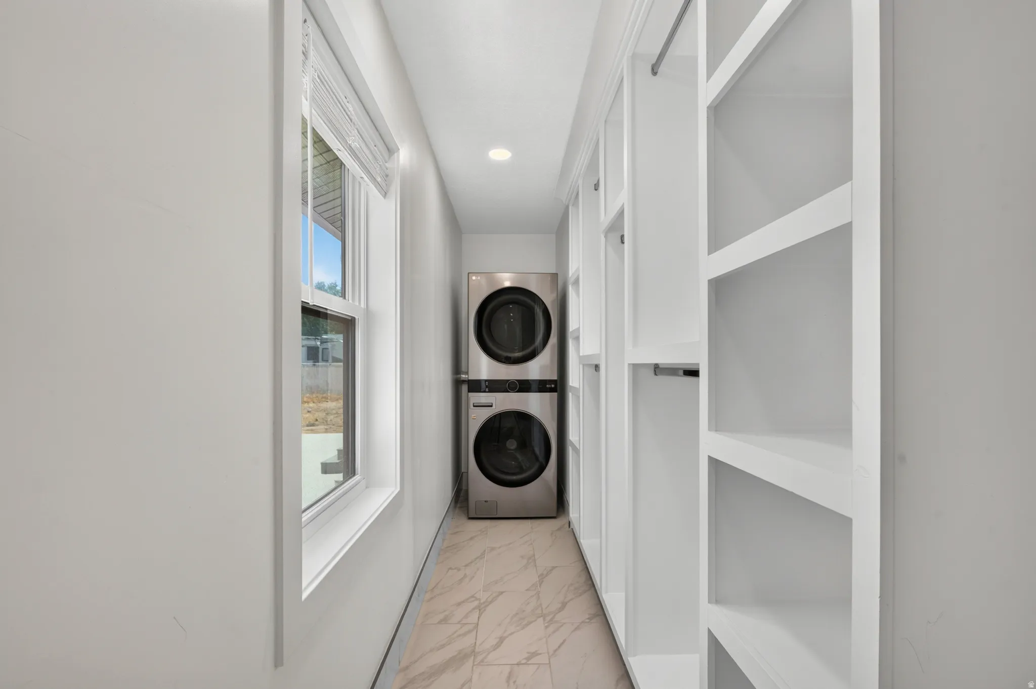 Dedicated laundry area featuring a stacked washer and dryer unit, built-in shelving, white walls, and light-toned tile flooring