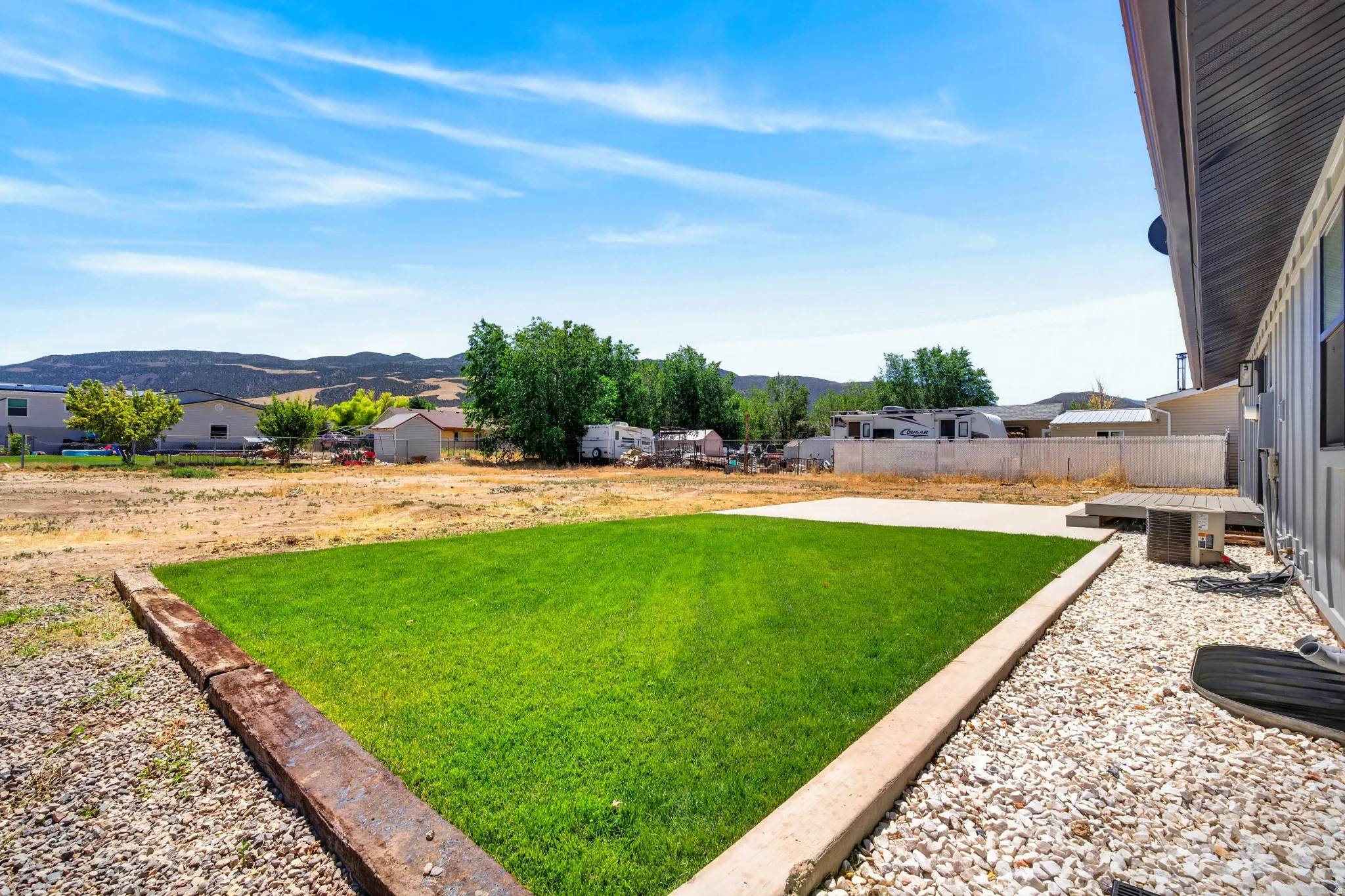 Expansive backyard featuring a manicured lawn, concrete patio, and gravel landscaping