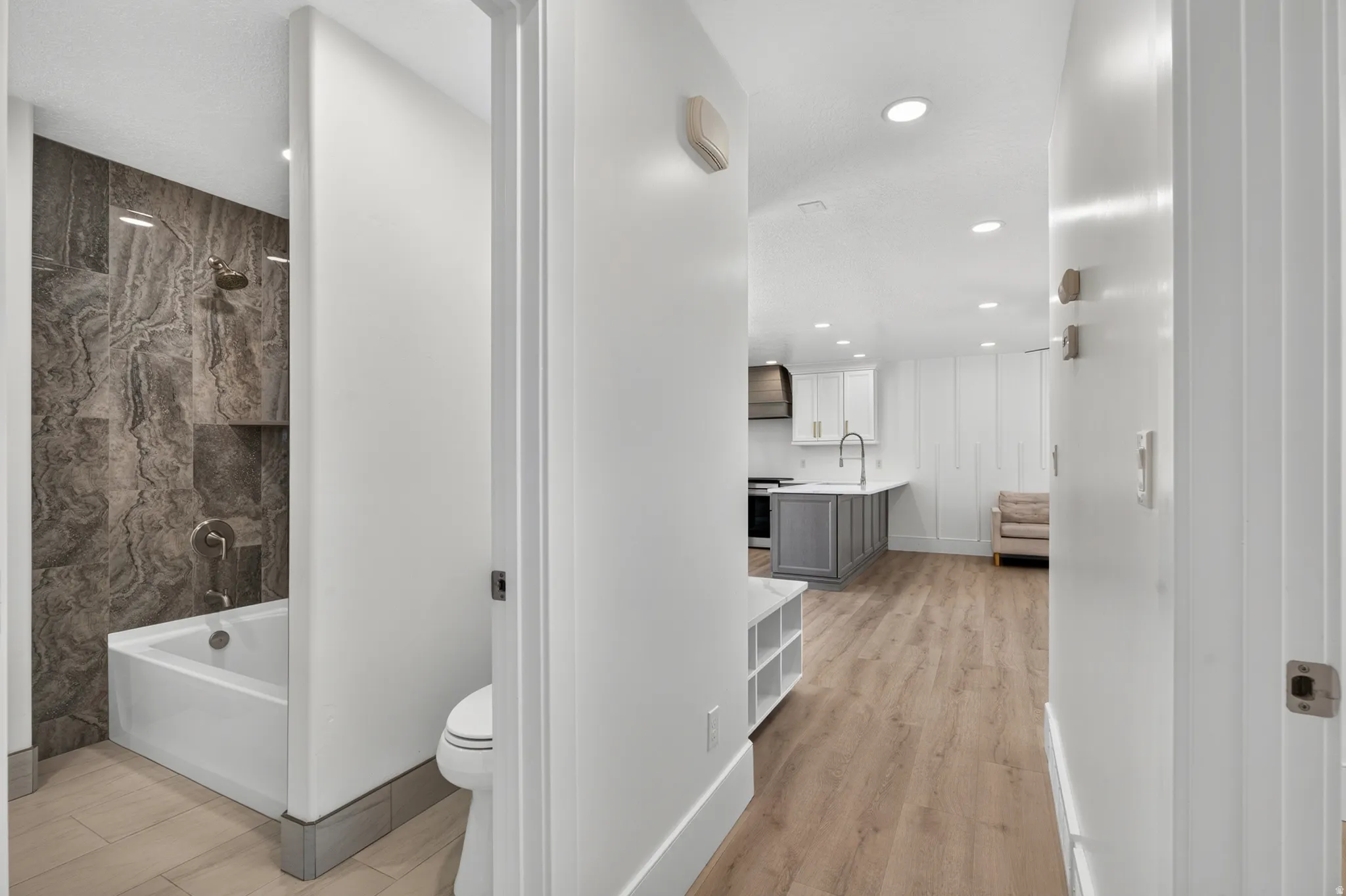 Full bathroom with a tub and shower featuring dark-toned patterned tile, built-in shower niche, and a contemporary toilet