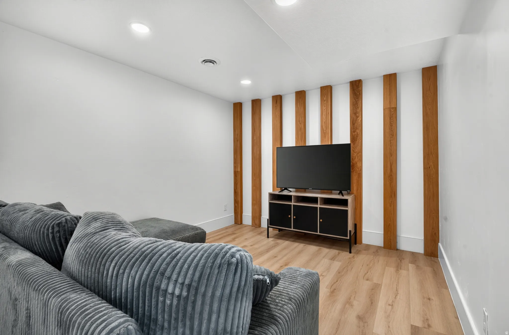 Living area featuring wood-finish flooring, recessed ceiling lighting, a contemporary wood accent wall, and white baseboards