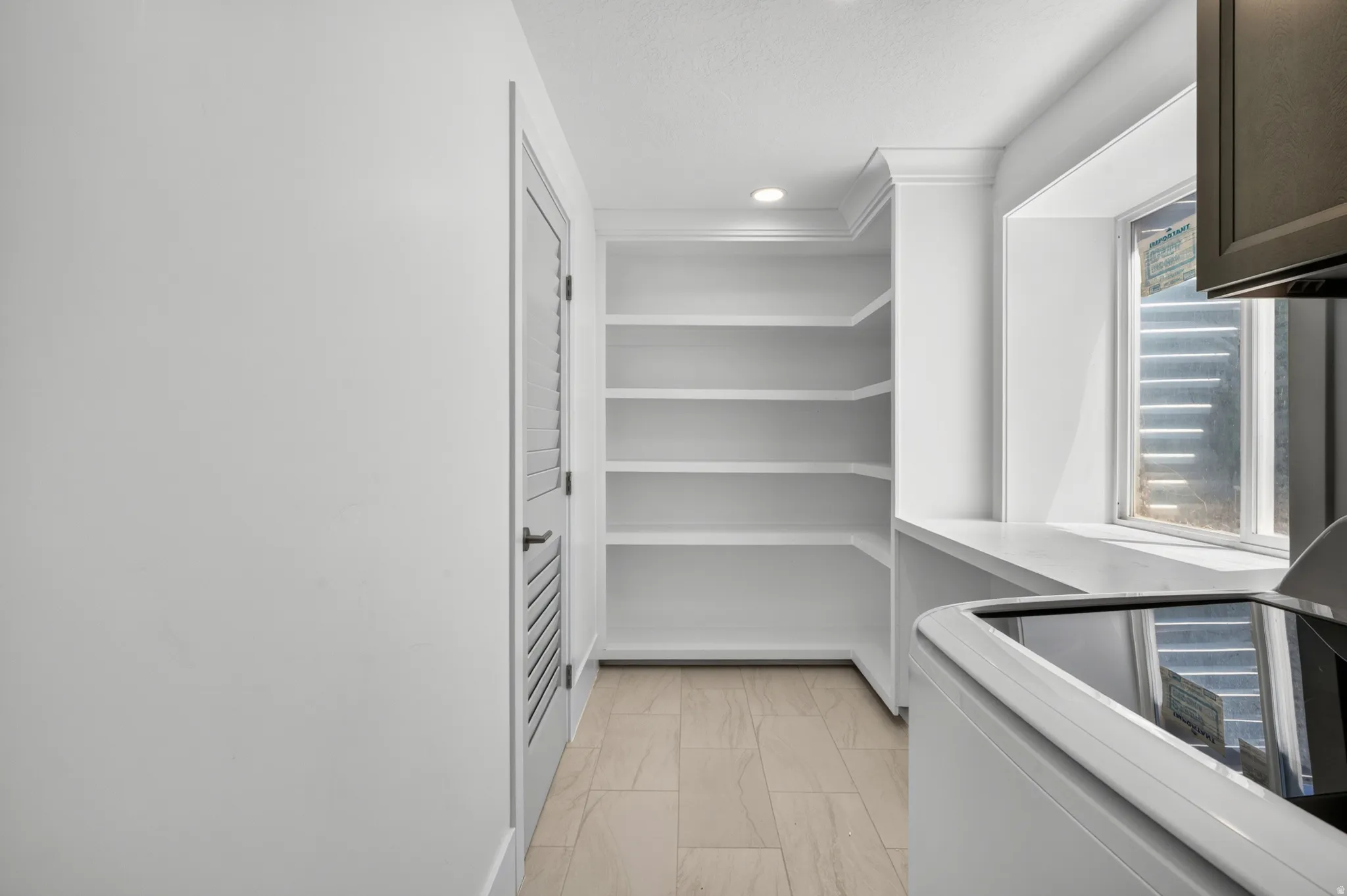 Built-in shelving unit, recessed lighting, window ledge, louvered door, and light-toned tile flooring