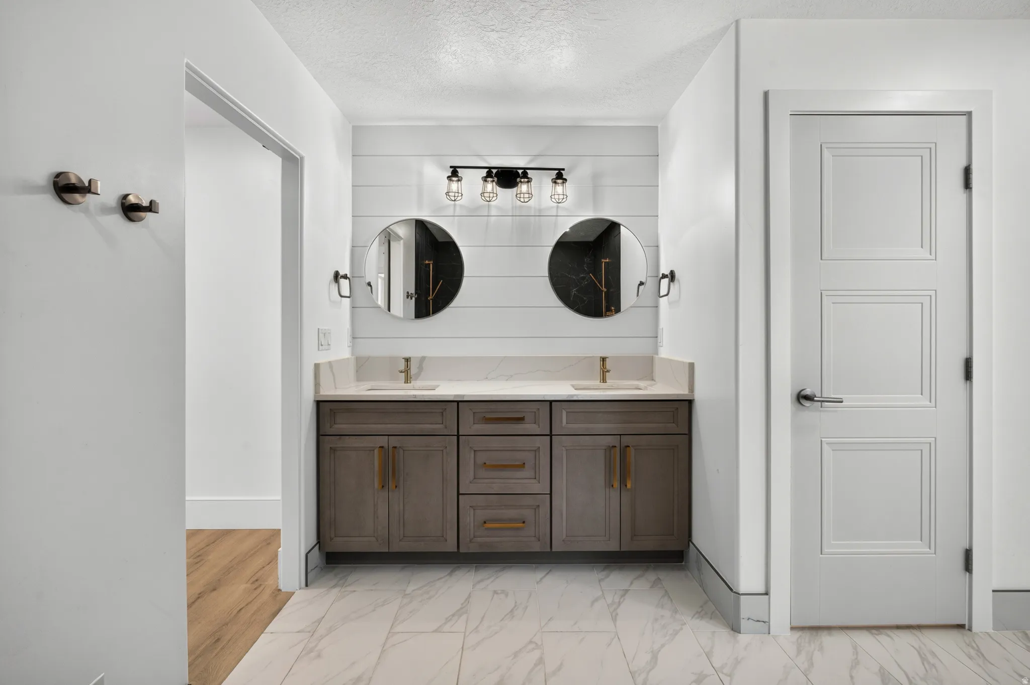 Bathroom featuring a dual vanity with a light-toned countertop, two integrated sinks with gold-toned fixtures, wood-finish cabinetry, and shiplap-style wall detailing