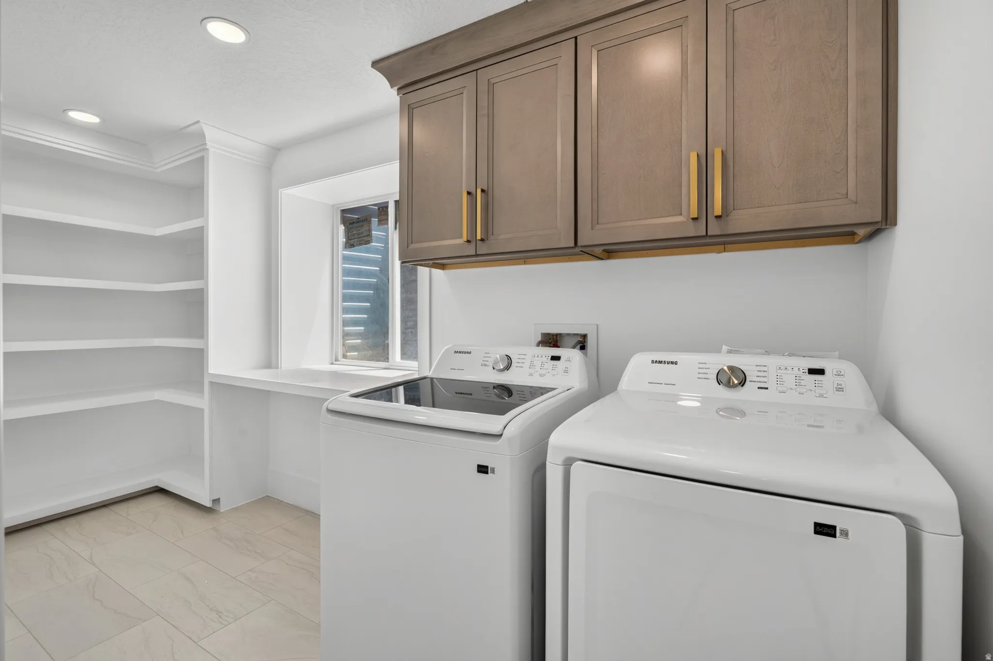 Dedicated laundry room featuring built-in shelving, a utility counter, recessed lighting, and upper cabinetry with gold-tone hardware