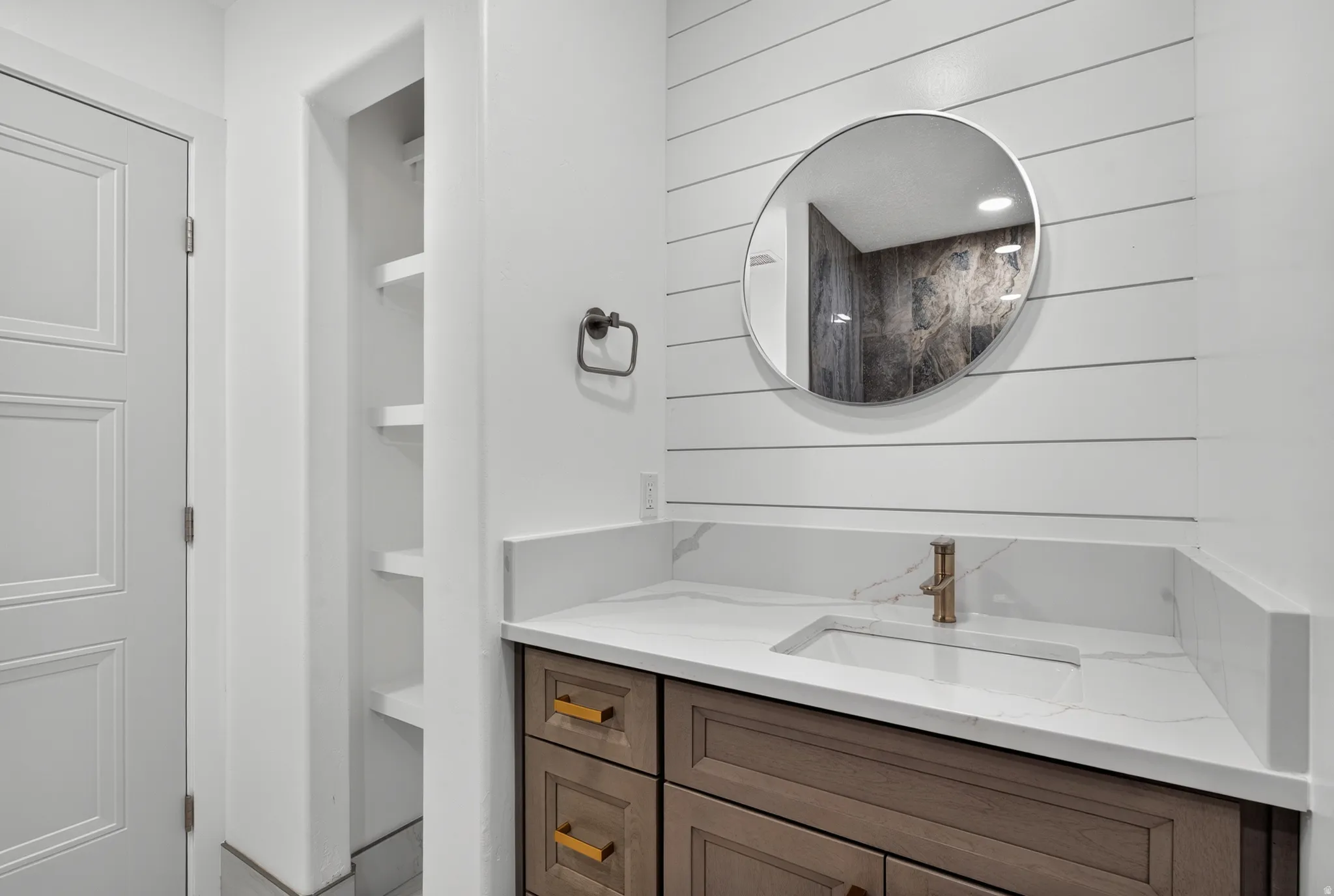 Bathroom vanity featuring a rectangular undermount sink, brass-finish faucet, and white stone-look countertop