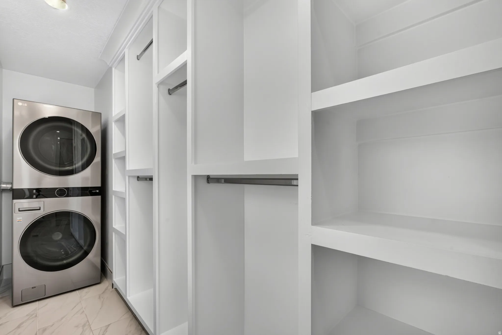 Dedicated laundry area featuring a stacked washer and dryer, custom white built-in shelving, and hanging rods