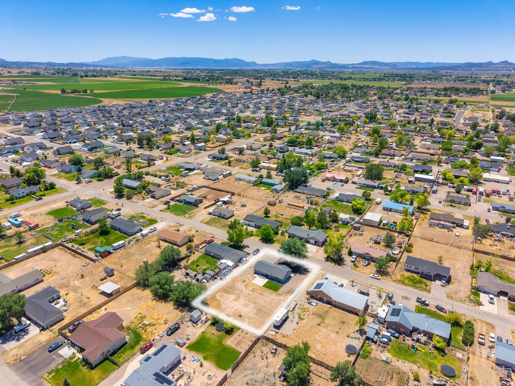 Aerial perspective showcasing a residential neighborhood with surrounding agricultural fields and distant mountains