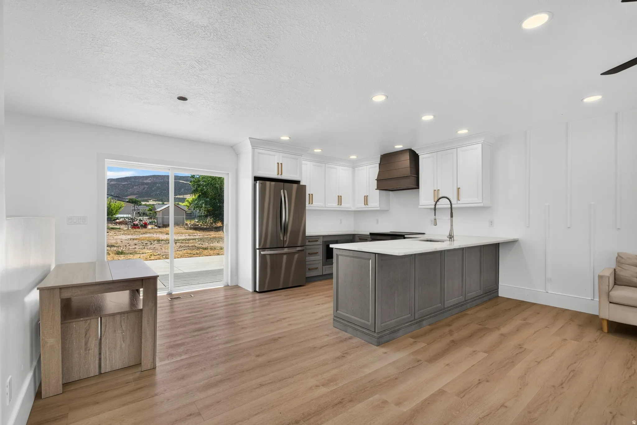 Open-concept kitchen featuring an island with a white countertop, two-tone cabinetry, stainless steel appliances, wood-finish flooring, and recessed lighting