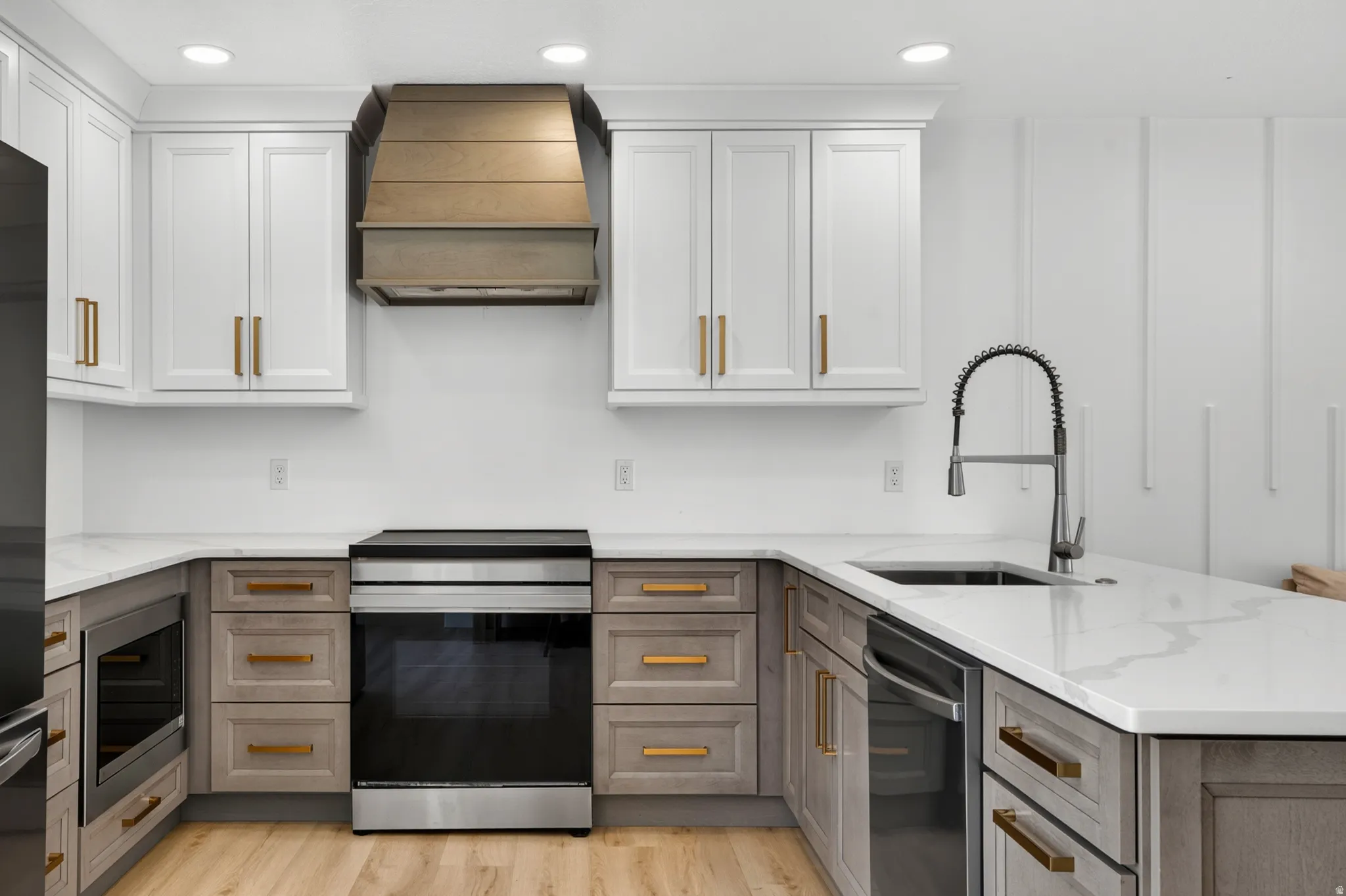 Kitchen featuring two-tone cabinetry with gold-finish hardware, quartz countertops, stainless steel appliances, and wood-finish flooring