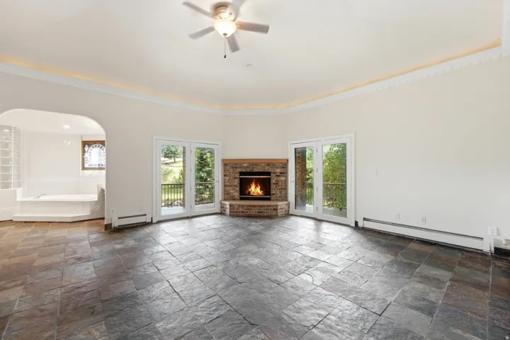 Spacious room featuring slate tile flooring, a corner brick fireplace, and two sets of glass-paned French doors