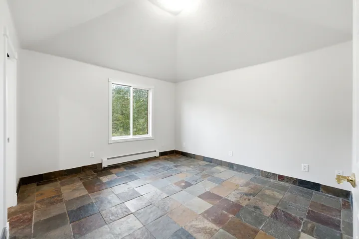 Spacious room featuring slate tile flooring, white walls, and a single window with a tree-lined exterior