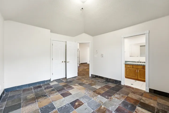 Spacious room featuring multi-toned slate tile flooring, white walls, and a vaulted ceiling