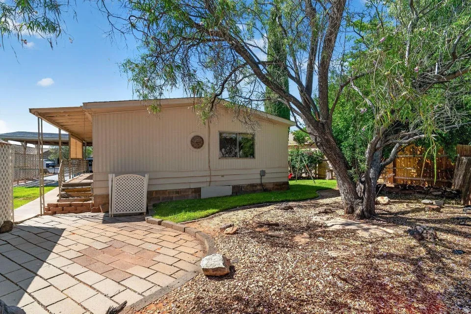 Exterior featuring a covered patio, brick-look paver pathway, and mature tree landscaping