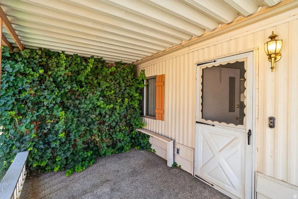 Covered entry area featuring a decorative screen door with X-panel design, a window with louvered shutters, and a brass-finish wall sconce