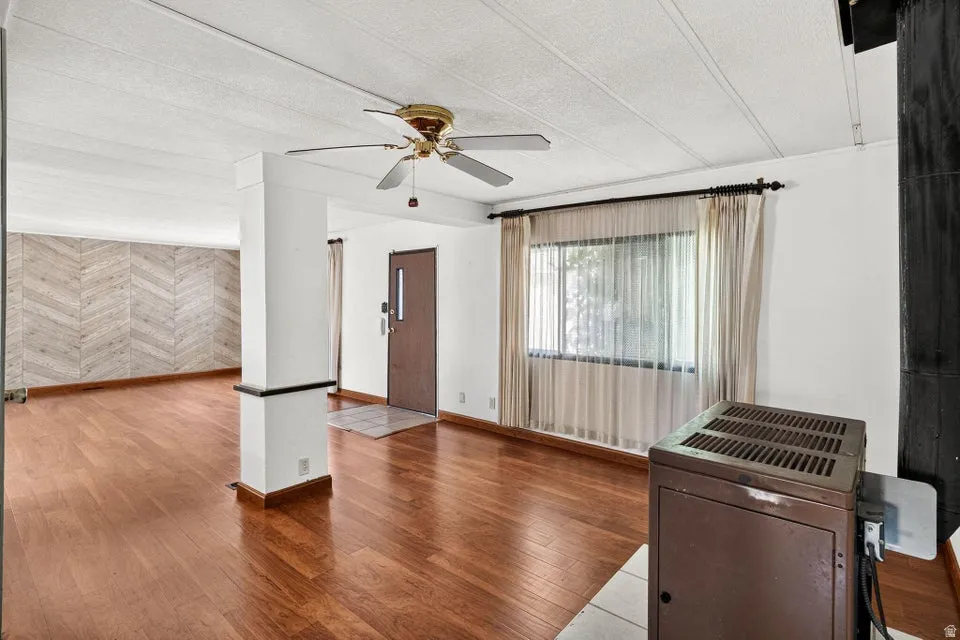 Open-concept living space with wood-finish flooring, a herringbone accent wall, and a ceiling fan