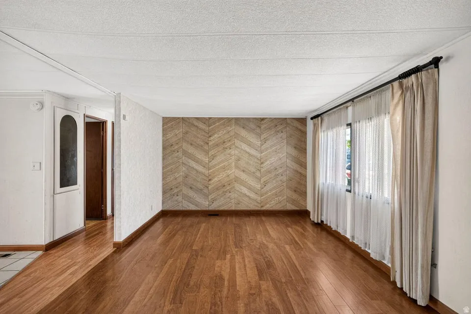 Wood-finish flooring throughout, complemented by a chevron pattern accent wall and a large window with sheers and drapes