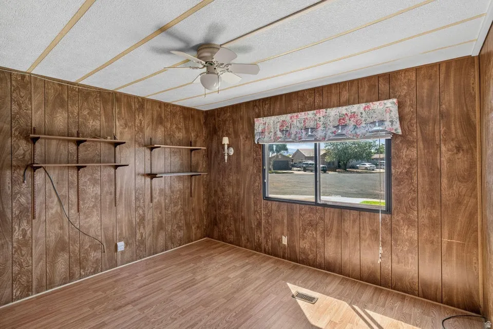 Interior room featuring wood-panel walls, wood-finish flooring, and a ceiling fan with integrated lighting