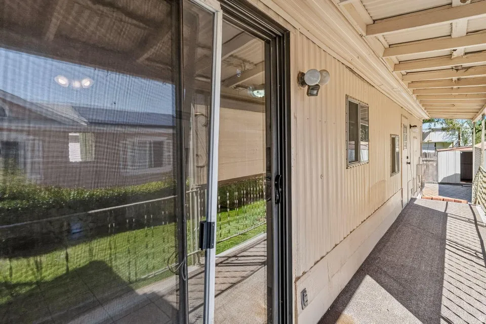 Exterior side porch featuring a sliding glass door, corrugated siding, outdoor lighting fixture, small windows, and a partially covered walkway with a ramp