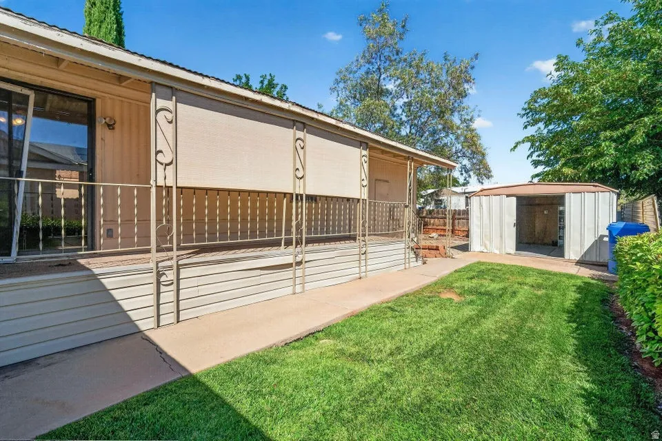 Outdoor space featuring a covered porch with decorative railing, sliding glass door access, a manicured lawn, and a metal storage shed