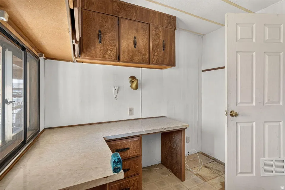 Functional workspace featuring a built-in U-shaped desk with a light-toned countertop, wood-finish cabinetry, and large sliding windows