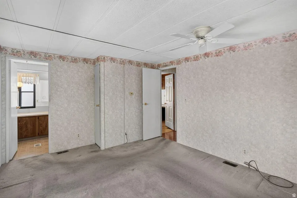 Carpeted room featuring a ceiling fan, two closet doors with brass-toned hardware, and textured wallpaper