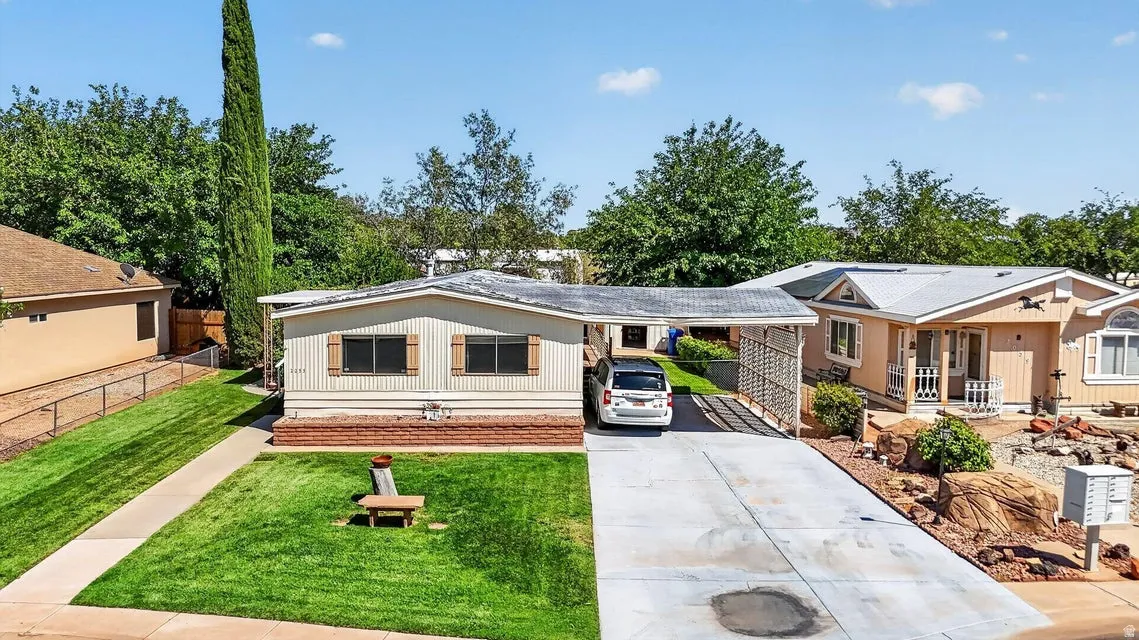 Single-story residence featuring a carport, a concrete driveway, a manicured lawn, and a brick-detailed foundation