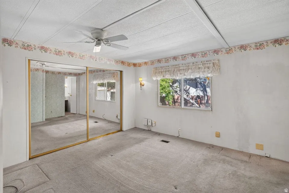 Room featuring a ceiling fan, mirrored closet doors, and a window with a valance
