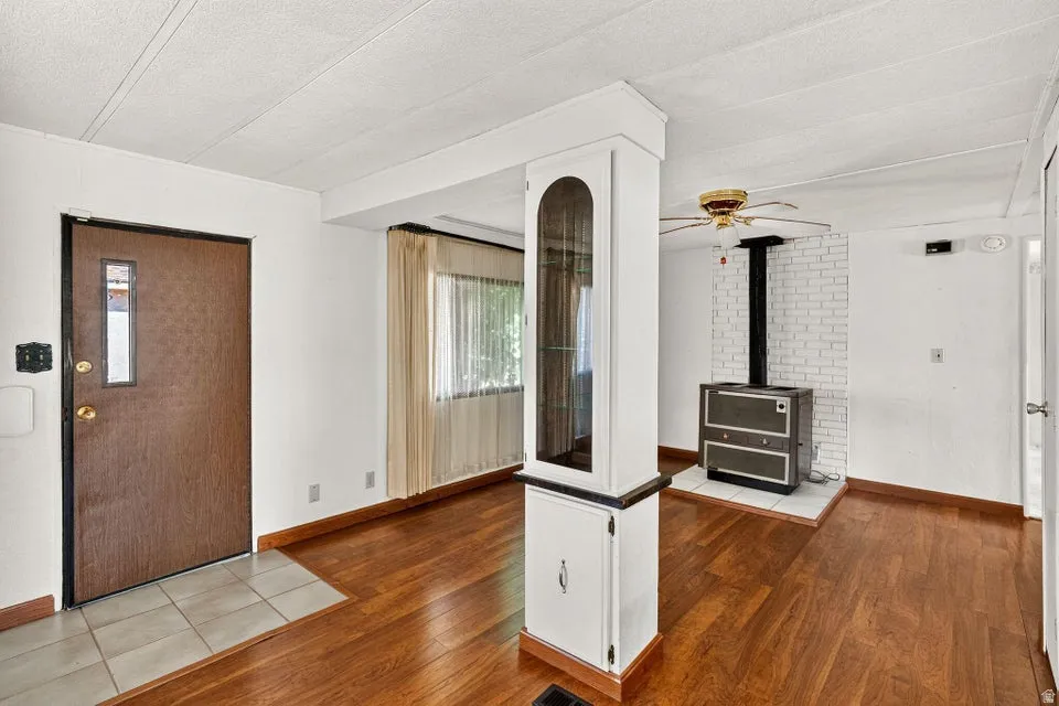 Interior featuring wood-finish flooring, a white brick-backed wood stove, and a ceiling fan